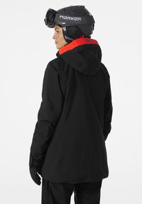 Black ski jacket with red hood accents, made of waterproof material. Features a relaxed fit and adjustable cuffs. Worn with a black helmet.