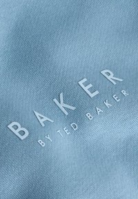 Hellblauer Stoff mit glatter Textur, auf dem in großen weißen Buchstaben "BAKER" und darunter in kleinerer Schrift "by TED BAKER" steht.