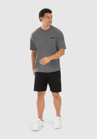 Camiseta gris de manga corta con logo negro, combinada con pantalones cortos negros y zapatillas blancas. Tela suave, corte relajado y diseño minimalista.
