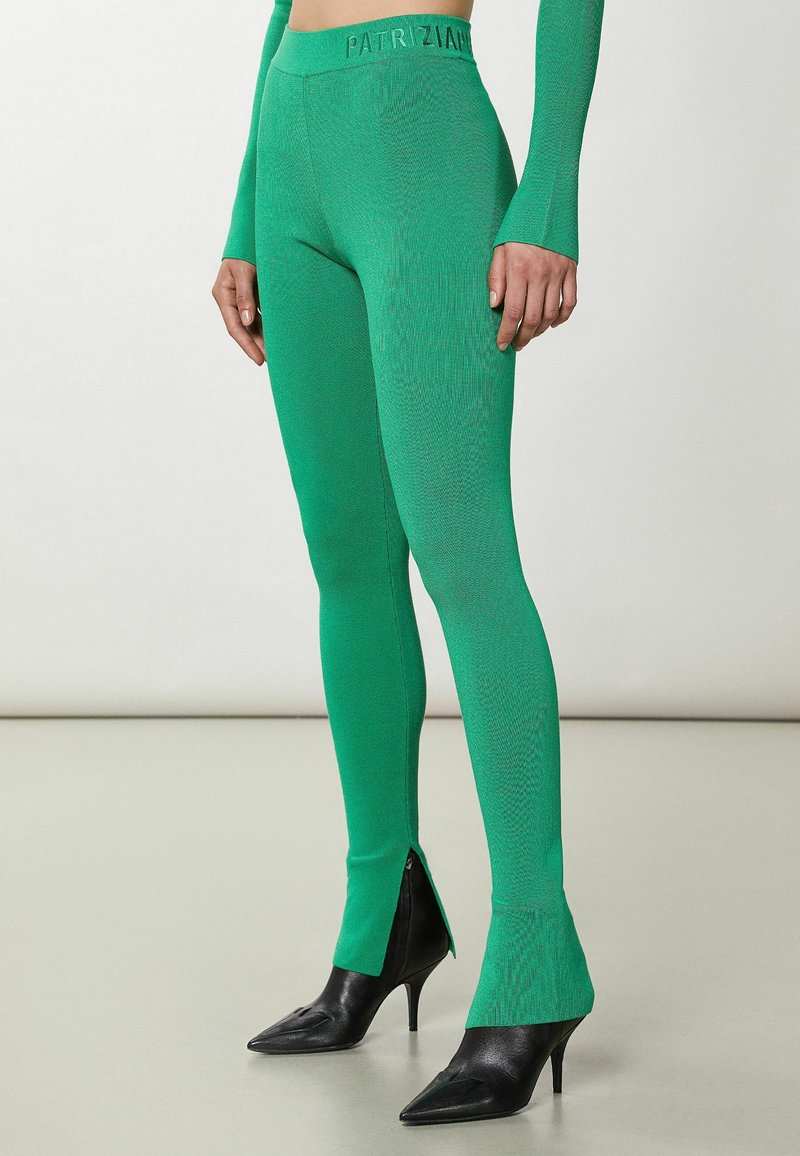 Groene gebreide leggings met een gestructureerd patroon en zijritsen, met een gemerkte tailleband. Gepaard met zwarte puntige hakken.