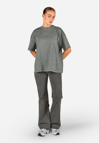 Przyduża szara bawełniana koszulka z krótkim rękawem i okrągłym dekoltem, zestawiona z szarymi dżinsami dzwonami i wielokolorowym obuwiem sportowym.