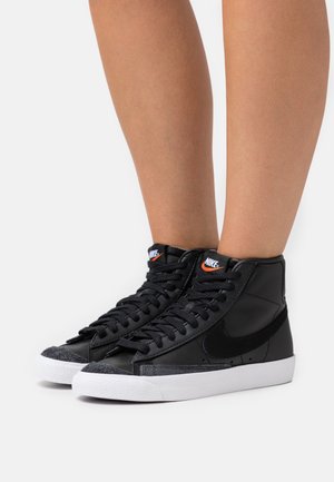 Czarne sneakersy z wysoką cholewką wykonane z gładkiej skóry, z teksturowanymi zamszowymi akcentami, białą gumową podeszwą oraz wyraźnym logo Nike na języku.