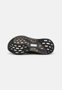 Semelle de chaussure de sport noire en caoutchouc texturé avec des découpes circulaires et ovales pour une meilleure adhérence. Talon renforcé et conception de la section médiane flexible.