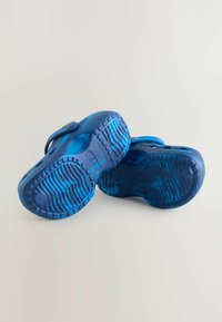 Blå slip-on skor med texturerade sulor, featuring en slät ovandel och luftiga utskärningar för ökad andningsförmåga. Lättviktig och flexibel design.