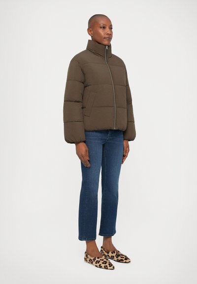 Giacca a vento marrone con colletto alto, chiusura a zip e due tasche laterali. Presenta sezioni trapuntate e una texture morbida. Abbinata a jeans blu e ballerine con stampa leopardata.