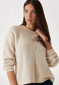 Cremefarbener gestrickter Pullover mit einem Zopfmuster und Blattdesign, gerippten Bündchen und rundem Ausschnitt. Weiche Textur und lässige Passform.