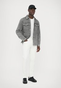 Szürke farmerdzseki klasszikus kialakítással, fehér pólóval, fehér nadrággal és fekete sportcipővel. A sapka fekete. Egyszerű és modern ruházat.