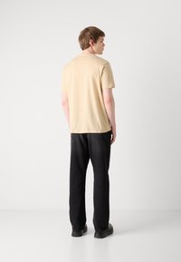 Beige bomulds T-shirt med korte ærmer, parret med sorte denim jeans. Bagfra viser snug pasform og simpelt design uden dekorationer.