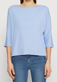 Top azzurro chiaro, morbido e oversize con scollatura ampia e maniche a tre quarti. Il tessuto sembra morbido con una sottile texture; design semplice e versatile.