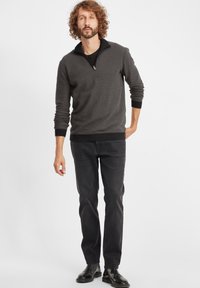 Mørk grå genser med teksturert mønster, glidelås i kragen og ribbestrikkede mansjetter. Kombinert med svarte, rette jeans og svarte støvler.