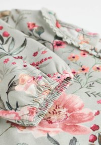 Bloemmotiefstof in zacht grijs, met levendige roze en gele bloemen. Samengestikte elastische details bij de manchetten met kantaccenten.
