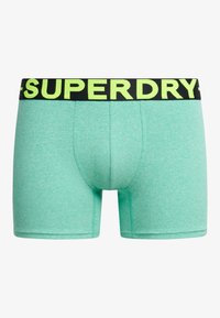 Bóxer verde menta con una cinturilla elástica negra y amarilla fluorescente con el logo 'SUPERDRY'. Material suave con una textura lisa y diseño ajustado.