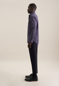 Camicia a fantasia navy, slim fit, maniche lunghe e dettagli con bottoni, abbinata a pantaloni e scarpe nere, mostrata di lato su uno sfondo neutro.