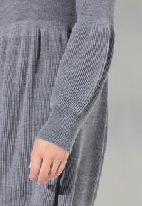 Robe en tricot côtelé gris avec une silhouette évasée et des manches longues. Le poignet est ajusté, et la texture est douce et lisse.
