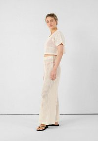 Crème-kleurige tweedelige set van gestructureerde breiwerkstof, bestaande uit een cropped top en lange, rechte broek met open gaasdetails.