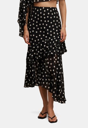 Black asymmetrical midi skirt with white polka dots and ruffled layered hem, worn with black strappy heeled sandals.
