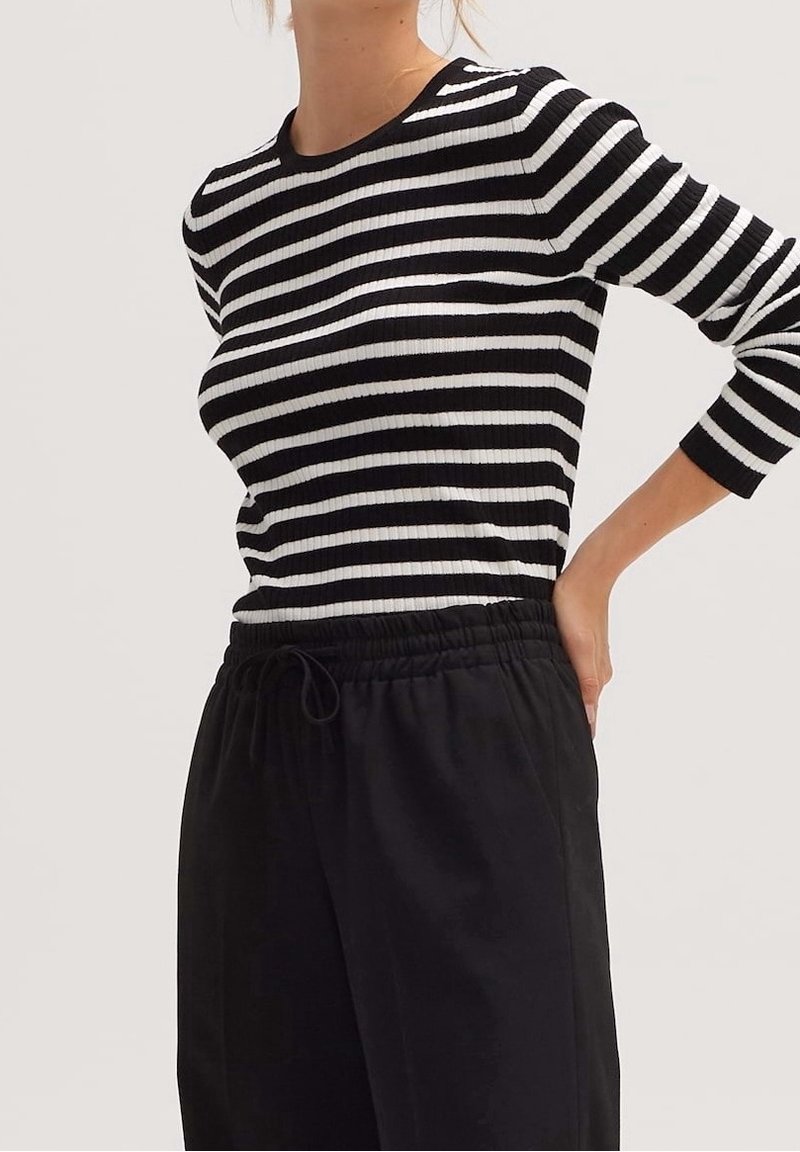 Czarno-biały prążkowany sweter w paski z rękawami do połowy przedramienia i okrągłym dekoltem, zestawiony z luźnymi czarnymi spodniami.