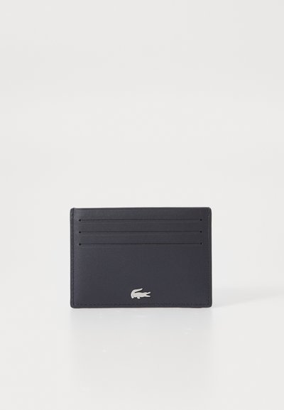 Porte-cartes en cuir bleu marine avec quatre emplacements pour cartes, une texture lisse et un petit accent logo argenté en bas.