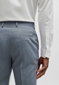 Light gray textured trousers with a flat front and back pocket, paired with a white long-sleeve shirt featuring buttoned cuffs.