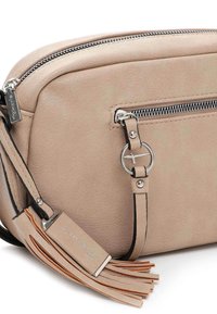 Beige läderaxelväska med silverfärgade dragkedjor, en rund hårdvaruaccent och dekorativa kvastar på sidan. Slät yta och kompakt design.