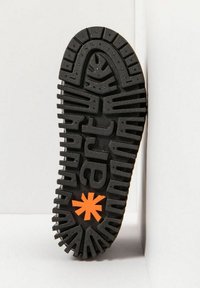 Suela de zapato de goma negra con profundas ranuras y un acento en forma de estrella naranja en el centro, con diversas estrías y crestas para mayor tracción.