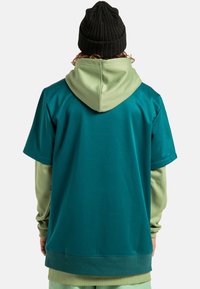 Turkusowa koszulka z krótkim rękawem nałożona na jas green koszulkę z długim rękawem, zestawiona z czarną dzianinową czapką. Gładka faktura, casualowy styl.