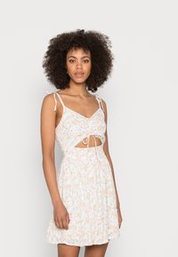 Vestido floral com base branca, flores laranja e amarelas, decote em V, alças ajustáveis, detalhe recortado na cintura e bainha ampla.