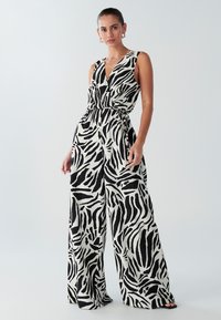 Zwart-witte jumpsuit met zebraprint, diepe V-hals, wijde pijpen en een ceintuur in de taille. Gemaakt van lichtgewicht stof met een gladde textuur.
