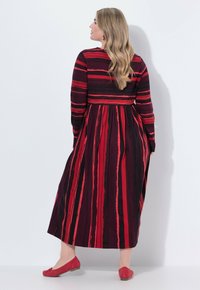 Maxikleid in Rot und Schwarz mit vertikalem Streifenmuster, langen Ärmeln, tailliertem Bund und fließendem Rock. Kombiniert mit passenden roten Ballerinas.