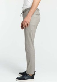 Gray tapered pants with a drawstring waistband, side pockets, and a back pocket, paired with dark sneakers. Smooth texture and modern fit.