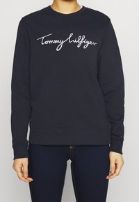 Marineblauwe sweatshirt met ronde hals, voorzien van een wit geborduurd "Tommy Hilfiger" logo op de voorkant en geribbelde boorden en zoom.