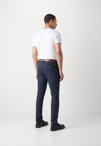 Pantalones ajustados azul marino hechos de una tela suave, con un cinturón marrón, dos bolsillos traseros y una silueta moderna.