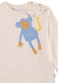 Hellbeige Langarmshirt mit einem blauen Affengrafik, einem orangefarbenen Gesicht, gelben Schwanzakzenten und einem Druckverschluss an der Schulter.