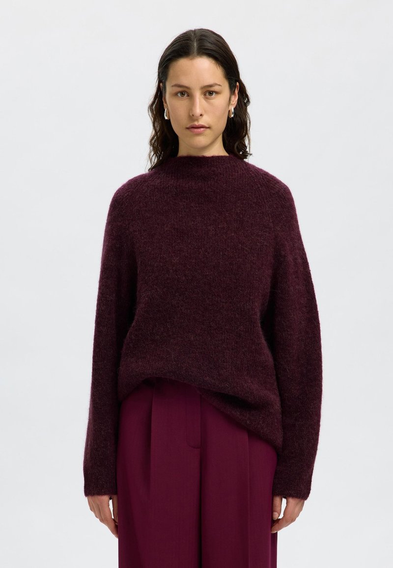 Pull en maille bourgogne avec un col haut, coupe ample et manches longues, assorti à un pantalon plissé. Texture douce, matériau chaud.