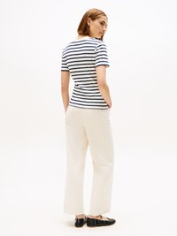 Camisa de manga curta às riscas em azul marinho e branco, combinada com calças largas em off-white e sapatos baixos pretos, apresentando um ajuste casual e descontraído.