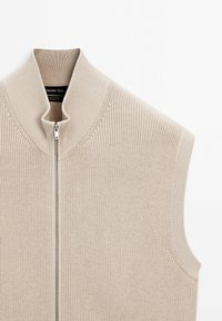 Beiger ärmelloser Pullover mit geripptem Muster, hohem Kragen, Metallreißverschluss, innen mit dem Etikett "Massimo Dutti", Baumwollmaterial.