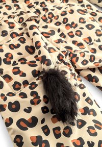 Leopardmönstrad tyg i beige med svarta och orange former. Inkluderar en lurvig svart svansdetalj; slät struktur med en glansig finish.