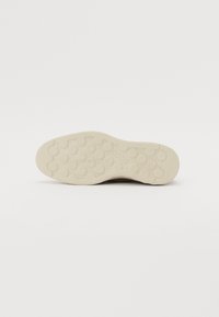 Lys beige gummisåle med nedsenkede sirkulære mønstre og teksturert overflate. Flat design med minimal slitasje for grep.
