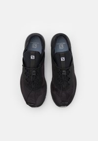 Chaussures de sport noires avec une tige en maille, des lacets élastiques et une semelle rembourrée. Possède un logo central et une silhouette épurée pour un confort optimal.