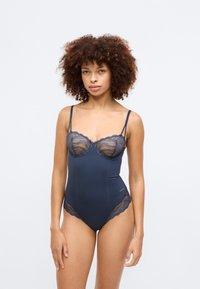 Tengerészkék bodysuit, csipke díszítéssel, kereknyakú és állítható pántokkal. Simább textúra, finom csipke részletekkel az oldalakon.