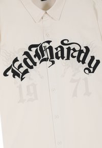 Biała koszula na guziki z czarnym gotyckim napisem "Ed Hardy" na piersi oraz delikatnymi szarymi nadrukami "1971" i smokiem poniżej.