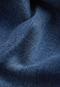 Primo piano di tessuto in denim blu scuro che mostra la trama dettagliata dell'intreccio e pieghe sottili.