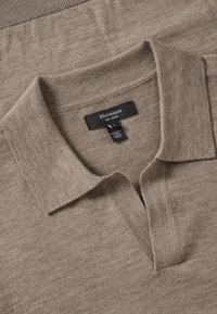Lichtbruine merinowollen polo met een zachte textuur, voorzien van een klassieke kraag en een label met de tekst "Matinique 100% Merino" aan de binnenkant.