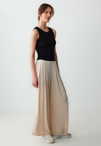 Zwarte, aansluitende tanktop gecombineerd met losse, beige palazzo-broeken. De outfit heeft een zachte textuur en een soepele draping. Witte sneakers maken de look compleet.