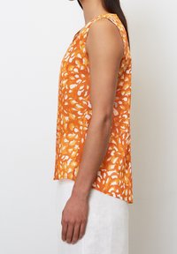 Top sin mangas en naranja con un patrón floral blanco, hecho de una tela ligera. Presenta un dobladillo recto y un corte relajado.
