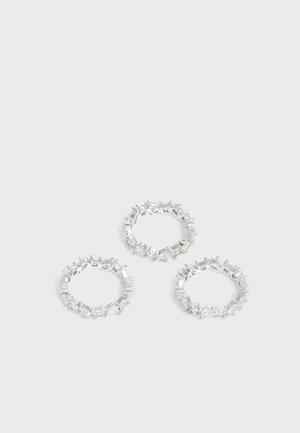 Trois bagues en argent avec plusieurs petites pierres précieuses transparentes rectangulaires et rondes disposées autour des anneaux sur un fond blanc.
