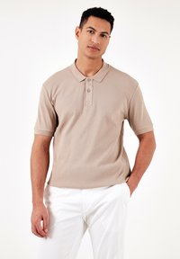 Beige raidallinen lyhythihainen polo paita, jossa on terävä kaulus, kaksinappinen nappilista ja hienovaraista ommelta edessä. Yhdistetty valkoisiin housuihin.