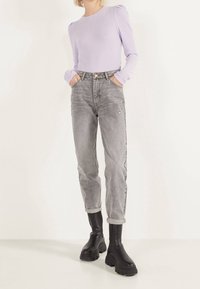 Top de manga larga de color púrpura claro con relieve combinado con jeans desgastados de cintura alta de color gris claro. Botines de tacón grueso y negro completan el atuendo.