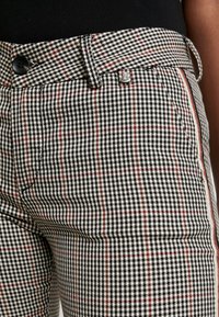 Pantalons à carreaux noir et blanc avec des accents rouges, dotés d'une fermeture à bouton, d'une coupe slim et de poches latérales. Tissu texturé avec un design structuré.