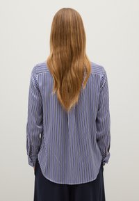 Camisa de manga larga a rayas en azul marino y blanco con dobladillo redondeado y puños abotonados, que presenta un canesú en la espalda y una textura suave.